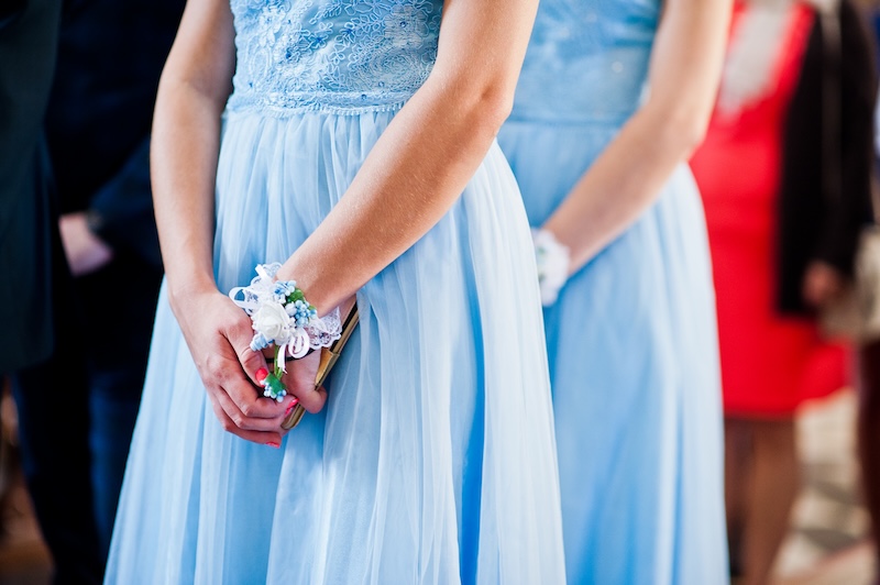 Zwei Frauen in hellblauen Spitzenkleidern mit passenden Ansteckblumen stehen nebeneinander und haben die Hände gefaltet.